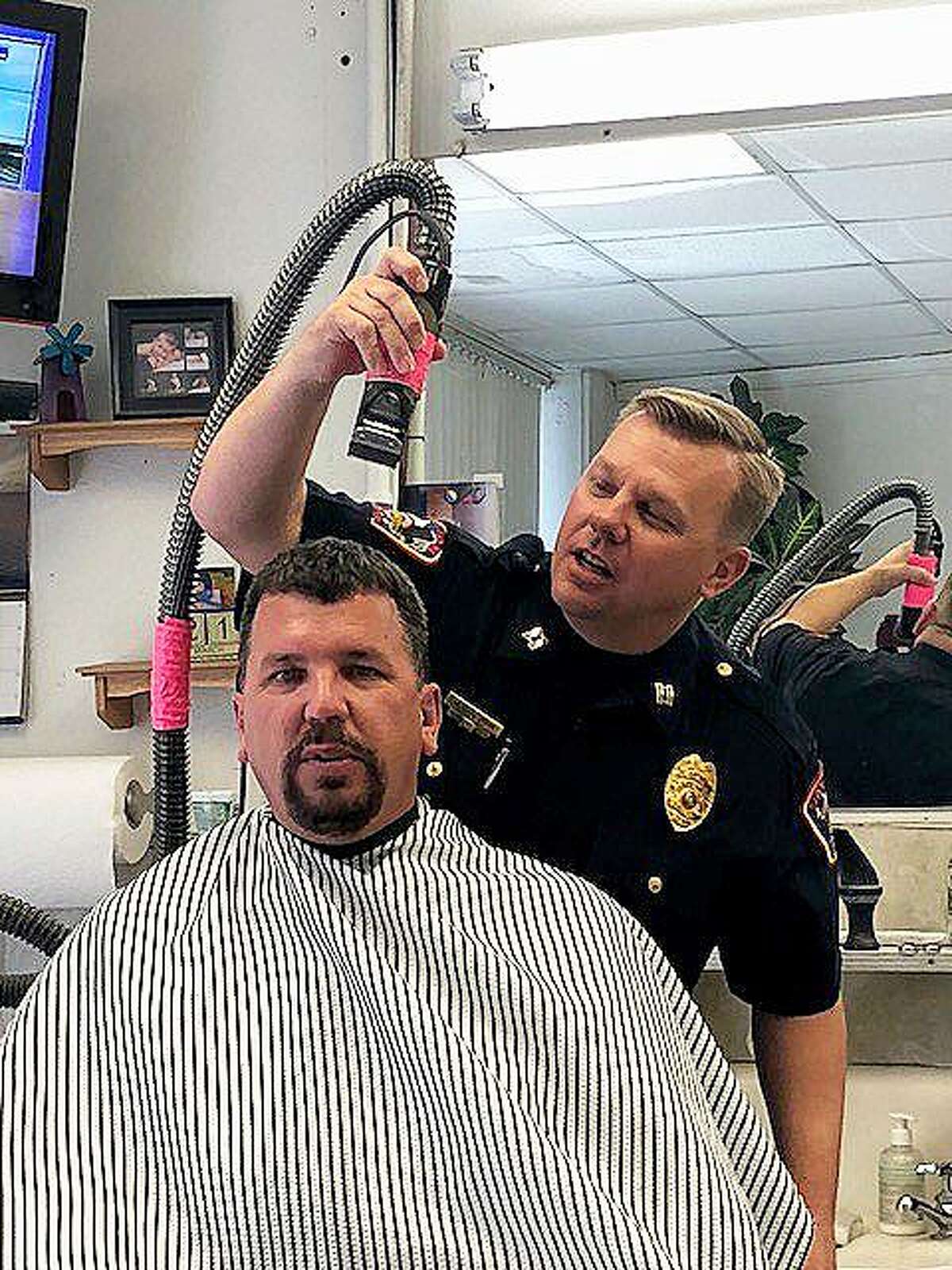 Capt. John Coleman holds the shears and begins to cut the hair of his Chief John Headrick. The two officers shaved their heads in support of Councilman Alvin Burress and his wife, Dana Shepard earlier this year.