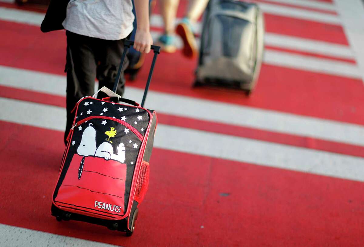 FILE - In this Nov. 22, 2017, file photo, a child pulls a suitcase along a crosswalk upon arriving at Hartsfield-Jackson Atlanta International Airport ahead of the Thanksgiving holiday in Atlanta. Parents may be feeling pressure to pay more money to sit with their young children on crowded planes despite a push by Congress to make airlines let families sit together at no extra cost. A consumer group has protested to Transportation Secretary Elaine Chao, asking her to begin writing regulations over the airlines?’ family-seating policies. (AP Photo/David Goldman, File)