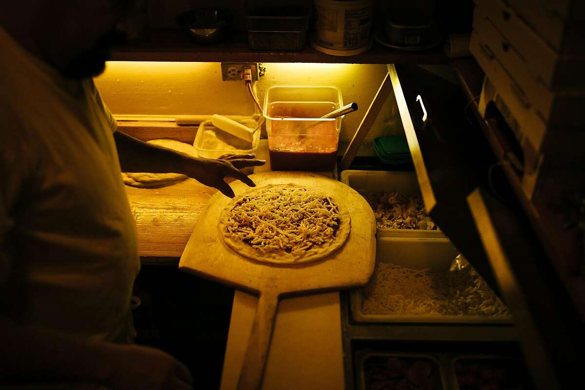 Rigoberto Rojas garnishes the pizzas before putting into the wood-fired brick oven at Tommaso's in San Francisco, Calif. Wednesday, December 6, 2017.
