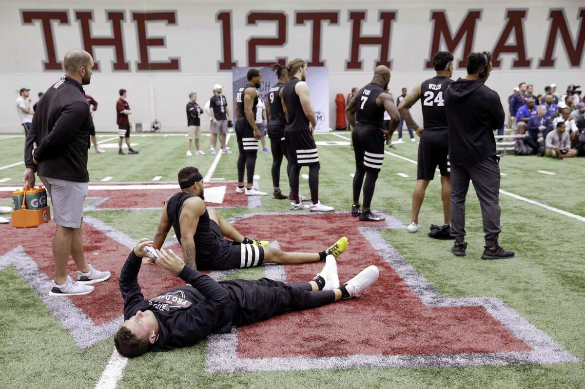 In this March 27, 2018 file photo, former Cleveland Browns quarterback Johnny Manziel lies on the turf looking at his phone between drills, with Texas A&M's "The 12th Man" trademarked nickname for its sports fans on the wall, rear, at his alma mater during football Pro Day in College Station, Texas. The school, among several that aggressively protects it's trademark, forced a man in nearby Bellaire, Texas, to stop producing a beer he called 12th Can saying it was too similar to 12th Man.