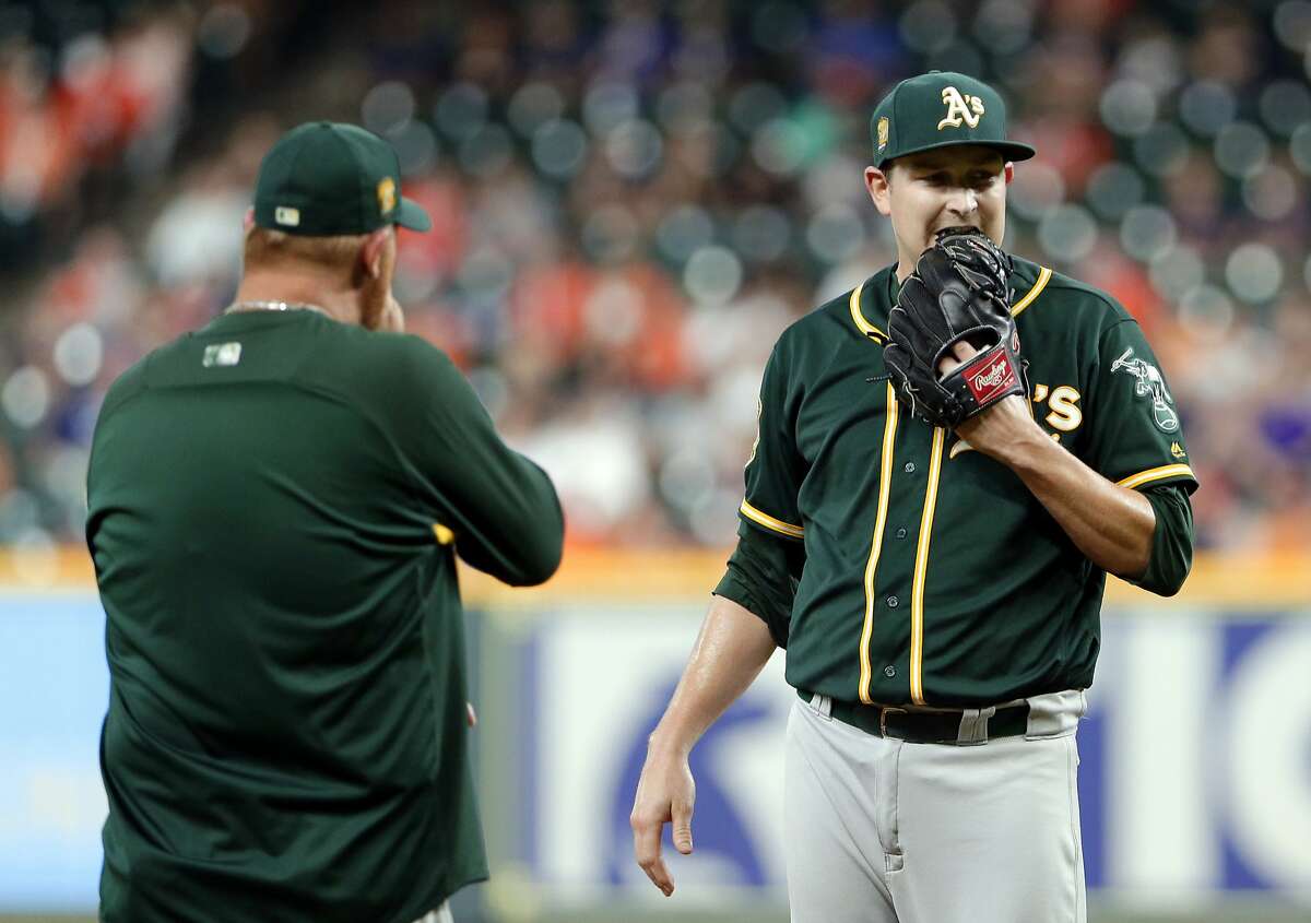 Oakland Athletics starting pitcher Trevor Cahill, right, bites his glove as pitching coach Scott Emerson, left, heads to the mound for a conference after the Houston Astros score two runs during the first inning of a baseball game Wednesday, Aug. 29, 2018, in Houston. (AP Photo/Michael Wyke)