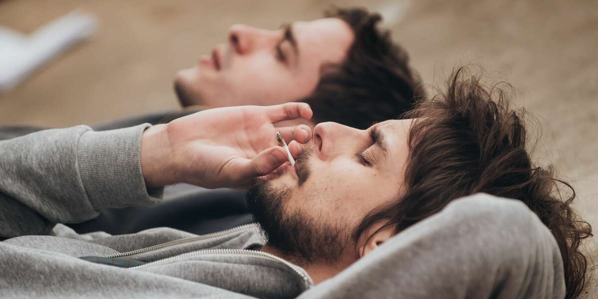 Two friends lying on the ground and smoking a joint.