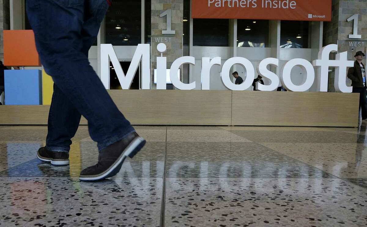 In this April 28, 2015, file photo, a man walks past a Microsoft sign set up for the Microsoft BUILD conference at Moscone Center in San Francisco. Microsoft says its requiring its U.S. suppliers to offer their employees at least 12 weeks paid leave to care for a new child. The company announced the new parental leave policy Thursday, Aug. 30, 2018.