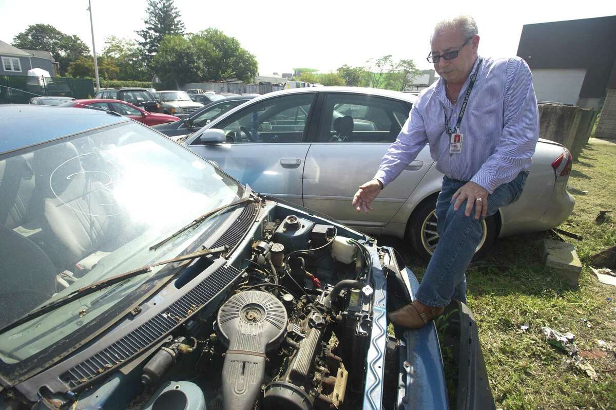 Fleet Manager Michael Scacco points to the engine of a car sitting in the city's fleet management lot on Magee Ave. after being abandoned and towed in Stamford, Conn. on Tuesday, Aug. 28, 2018. The car was left in this stripped condition before being towed to the lot and will soon be auctioned off for parts.