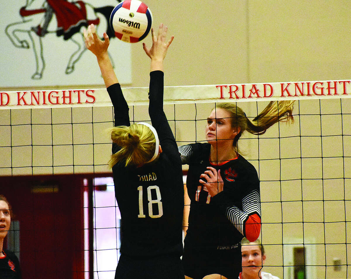 Edwardsville’s Storm Suhre, right, slams a kill through the Triad block during the first game on Monday inside Rich Mason Gymnasium in Troy.
