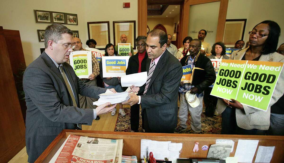 Rev. Abraham Hernandez, center, hands a stack of petitions to Sean Matteson, left, former New Haven Mayor John DeStafano's chief of staff, as a group delivered the petitions asking that Yale Hospital honor its agreement to hire 400 local residents. The mayor was not in his office to receive the petitions.