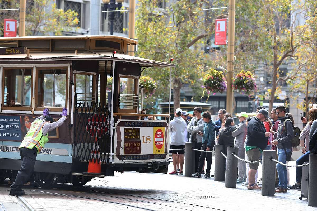 A cable car conductor helps turn a cable car next to people waiting in ine to board a cable car at Powell and Market Streets on Monday, September 17, 2018 in San Francisco, Calif.