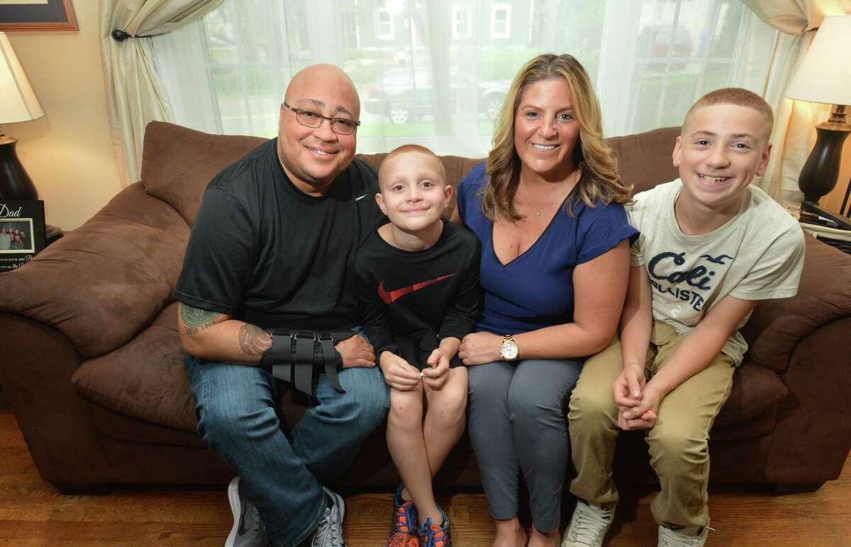 Patrolman Phil Roselle, at his Norwalk Conn. home on Monday September 17, 2018 with his wife Debbie and two of his sons, 9 year-old Ryan and 14 year-old Michael. Roselle, a 30-year veteran of the Norwalk Police Department, has been off the job for a year after an accidental discharge by another at the police shooting range left him with a bullet lodged in his rib and nerve damage to his right arm, and many other health issues and costs as his work benefits from the city have ended.