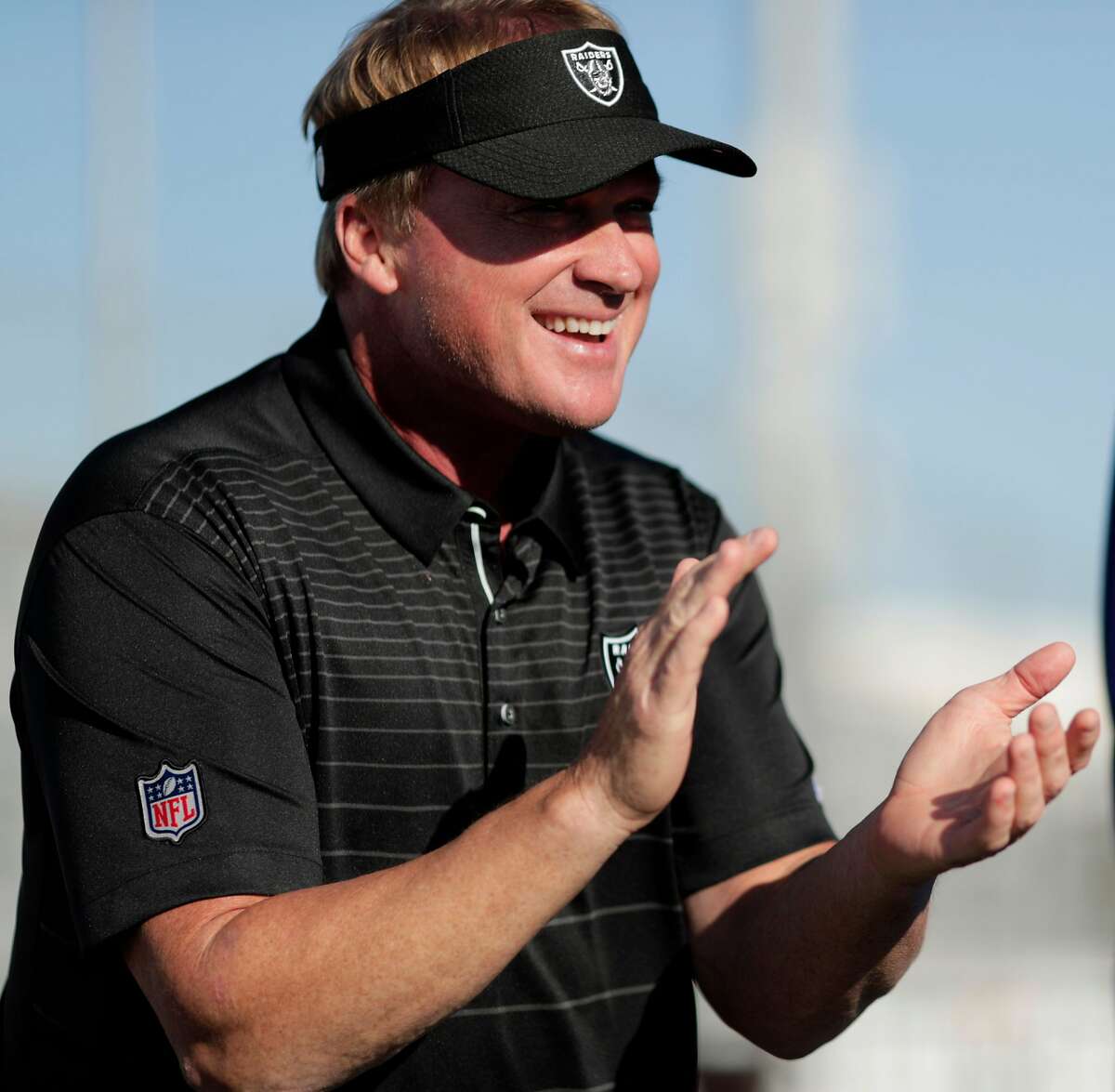 Oakland Raiders head coach Jon Gruden claps as kids pick up equipment and encouragement he delivered to about 60 kids from the San Leandro Crusaders and the East Bay Panthers at Burrell Field in San Leandro, Calif., on Tuesday, July 17, 2018. The gear, and $50000 was a joint donation of the Dick's Sporting Goods Foundation and Coach Gruden.