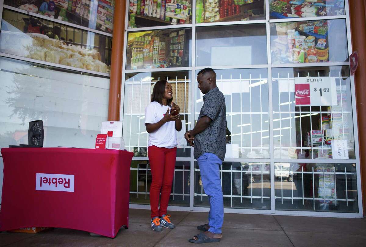 Tolulope Aladejobi, a Rebtel "activist," the term the company uses for their on-the-street sales representatives, works with Lucky Uwaifo to update his Rebtel app outside of the Southwest Farmers Market, Wednesday, Aug. 22, 2018 in Houston. Rebtel is a Swedish company that has a phone application allowing affordable international calling and soon will be able to transfer money internationally.