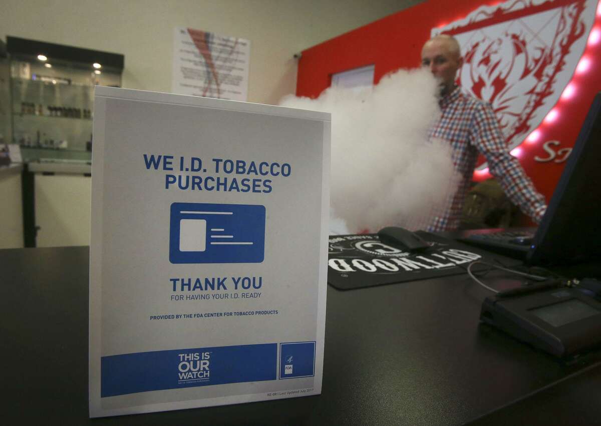 A sign on the counter at the Smoke to Live vape shop at 18154 Blanco Road reminds customers Thursday April 19, 2018 that tobacco products cannot be sold to people under the age of 18. Retailers, convenience stores, and smoke shop owners are preparing for the October 1 implementation of San Antonio's ordinance raising the tobacco buying age to 21. Vaping (right, background) is store manager Jordan Studer.