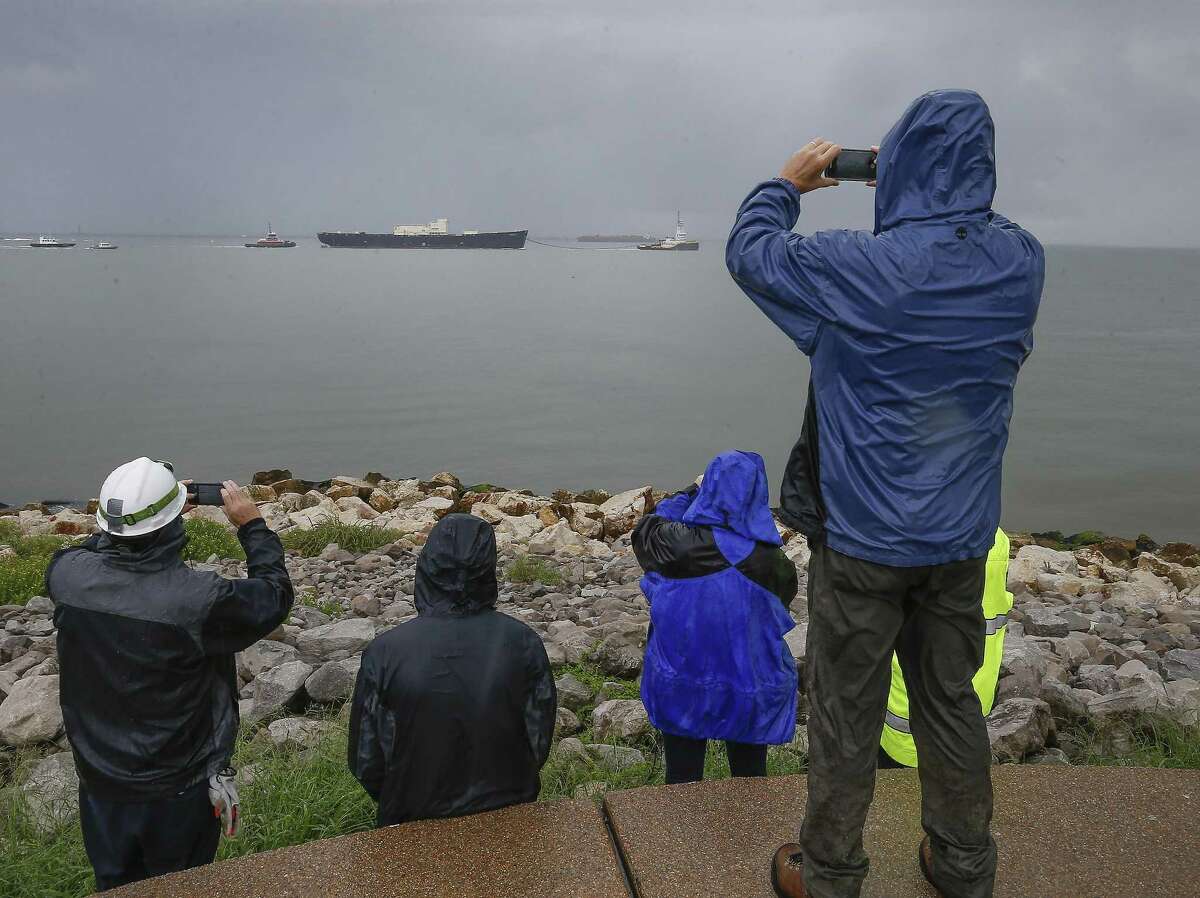 During a heavy rain shower, people take photos as the U.S. Army Corps of Engineers' STURGIS makes her way out of the Galveston shipping channel on her way to Brownsville Tuesday, Sept. 25, 2018, in Galveston.