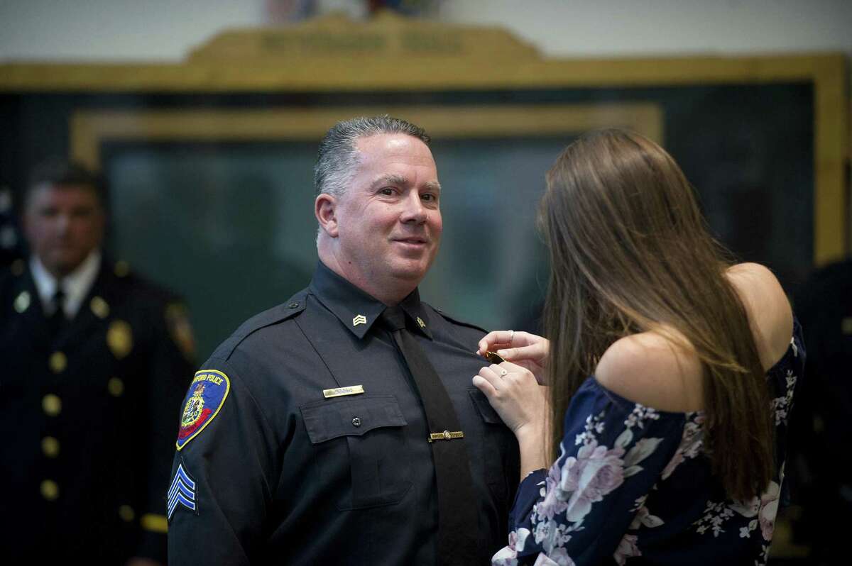 Sergeant Jeffrey Booth has a new badge pinned to his uniform by his daughter Emily Booth, 18, during the police promotion ceremony inside Government Center in downtown Stamford, Conn. on Tuesday, Sept. 25, 2018.