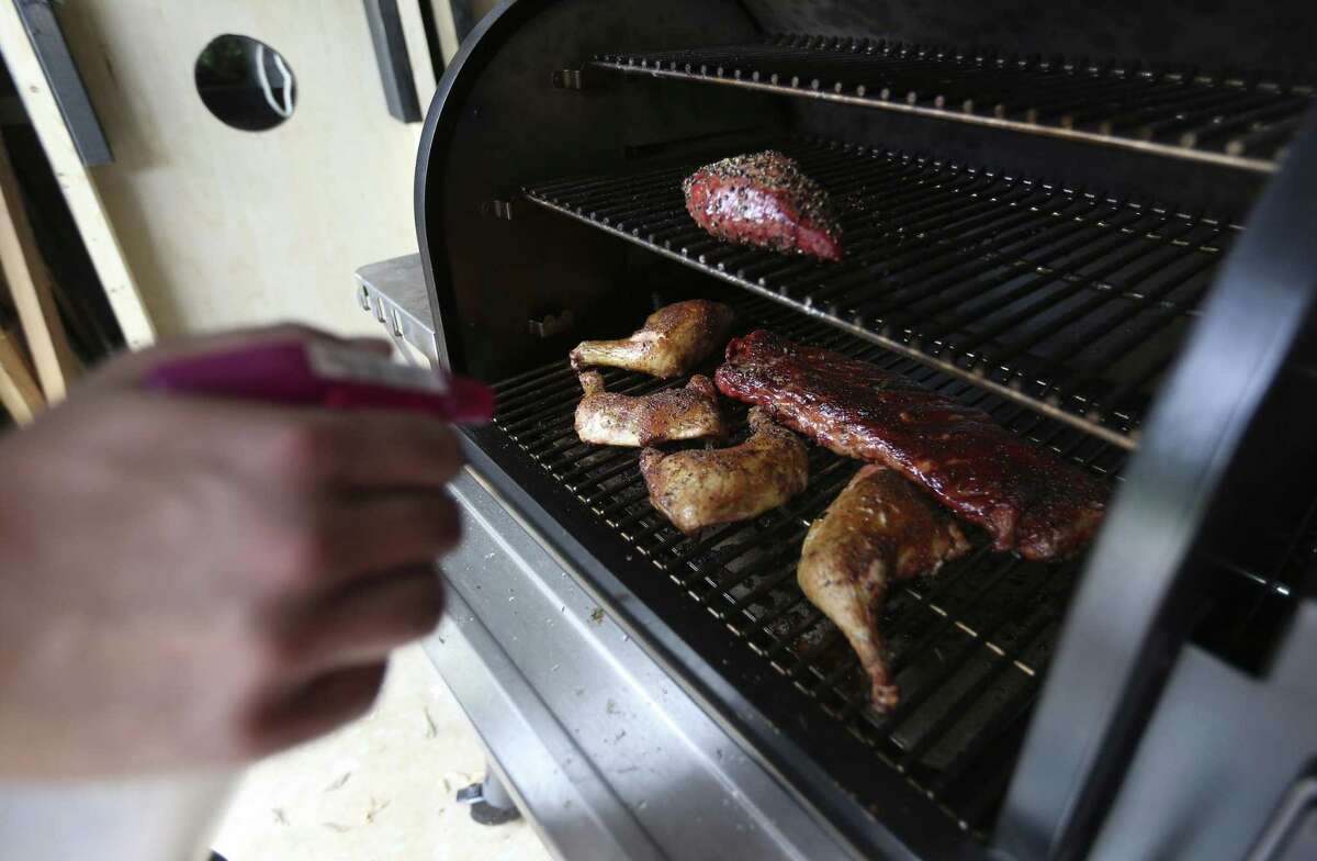 Finished chicken, ribs and beef tri-tip are seen being cooked in a pellet grill.