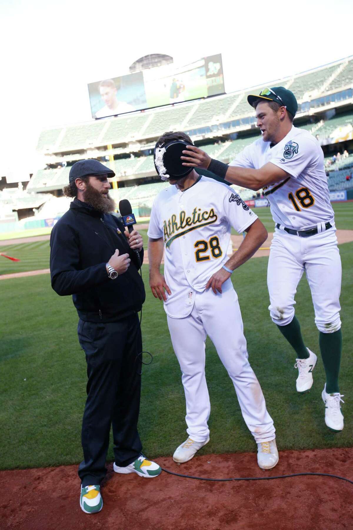 OAKLAND, CA - APRIL 18: Matt Olson #28 of the Oakland Athletics gets pied by Chad Pinder #18, while being interviewed by NBC Sports California Analyst Dallas Braden, after hitting a walkoff single following the game against the Chicago White Sox at the Oakland Alameda Coliseum on April 18, 2018 in Oakland, California. The Athletics defeated the White Sox 12-11. (Photo by Michael Zagaris/Oakland Athletics/Getty Images) *** Local Caption *** Matt Olson;Chad Pinder;Dallas Braden