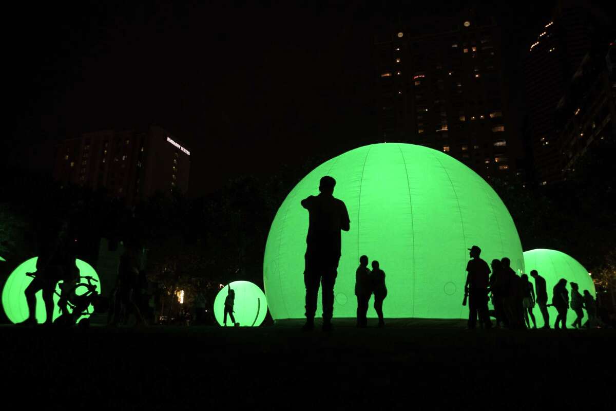 Visitors create silhouettes as they walk to observe the “moonGARDEN” spheres at Discovery Green. The installation will run until October 7th on the park.