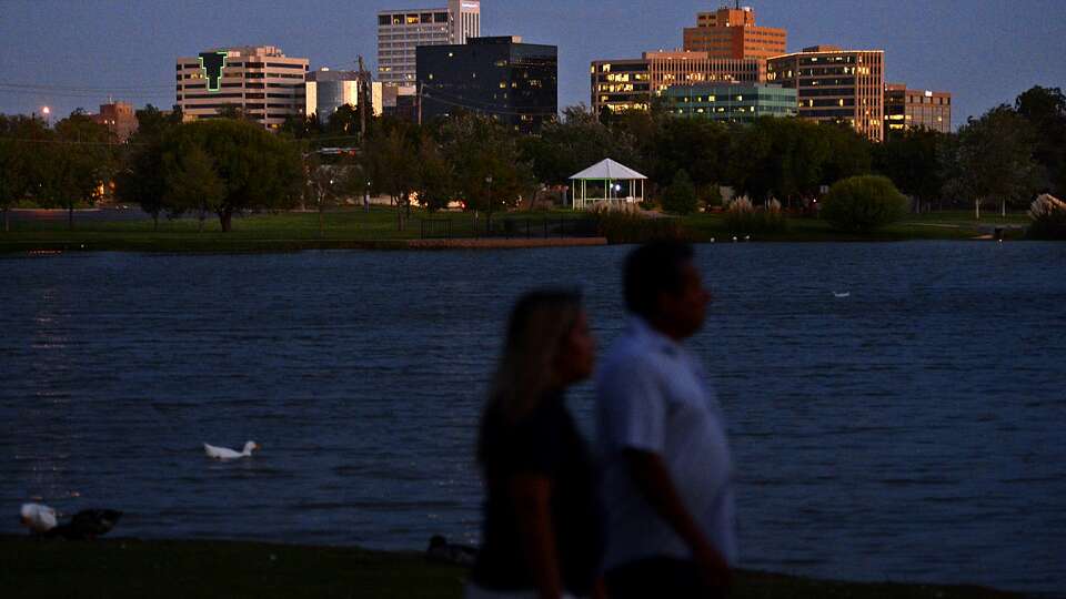 The Midland skyline is visible as a couple walks around the pond after sunset at Wadley-Barron Park, Oct. 3, 2018. James Durbin/Reporter-Telegram