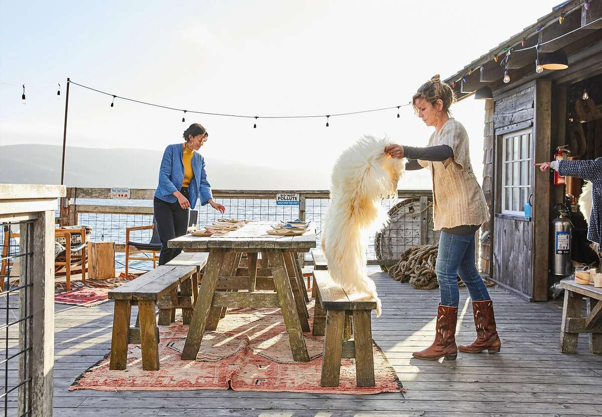 Kelli Dunaj (left) of Spring Coyote Ranch adds one of her sheepskins to the bench before a West Marin makers dinner at the boat house at Nick�s Cove on Tomales Bay on Thursday, Sept. 13, 2018 in Marshall, CA. The makers all know each other and contributed something from their craft to the meal.