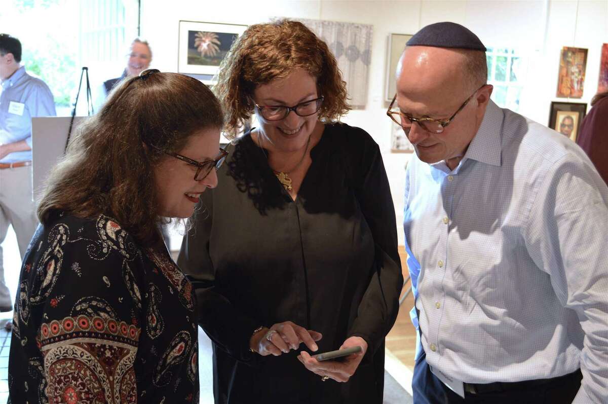 Nancy Mimoun, center, shares pictures with Elissa and Philip Klapper, all of Stamford, at the United Jewish Federation of Greater Stamford, New Canaan and Darien's Major Donor Reception at the Carriage Barn Art Center, Sunday, Oct. 7, 2018, in New Canaan, Conn.
