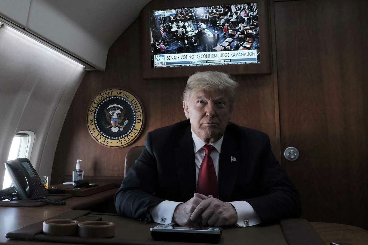 President Donald Trump speaks to reporters aboard Air Force One while a television shows the Senate as they vote on the confirmation of Judge Brett Kavanaugh to the Supreme Court, at Joint Base Andrews in Maryland, Oct. 6, 2018. Trump was headed to a campaign rally in Kansas on Saturday as a deeply divided Senate was poised to confirm Kavanaugh. (Pete Marovich/The New York Times)