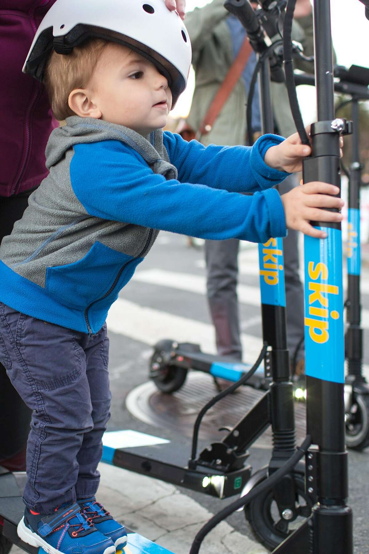 Milo, 23 months, stands on a Skip scooter held by his mom Susan Kimberlin at the demonstration booth of Skip, a scooter rental company, at the Castro Farmers' Market. Wednesday, October 10, 2018 in San Francisco, Calif.