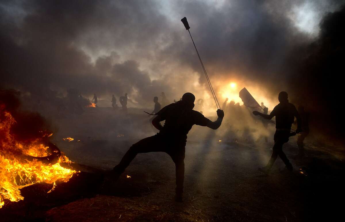 Black smoke from burning tires covers the sky over Palestinian protesters hurl stones toward Israeli troops during a protest at the Gaza Strip's border with Israel, Friday, Oct. 12, 2018. (AP Photo/Khalil Hamra)