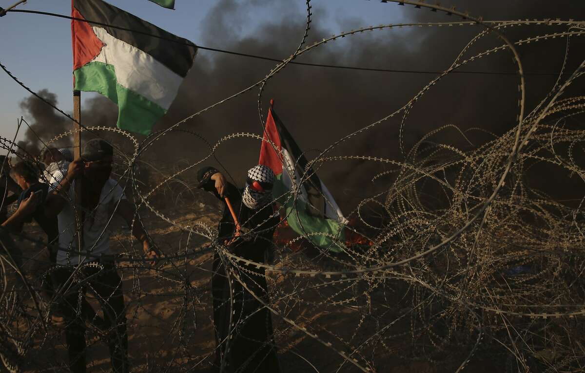 Protesters cut the border wire while others burn tires near the fence of the Gaza Strip border with Israel during a protest east of Khan Younis, southern Gaza Strip, Friday, Oct. 12, 2018. The Israeli military said 14,000 Palestinians thronged the border fence areas, burning tires and throwing rocks, firebombs and grenades at soldiers stationed atop earth mounds on the other side of the barrier. Since March, Hamas has orchestrated near-weekly protests along the fence, pressing for an end to a stifling Israel-Egyptian blockade imposed since the militant group wrested control of Gaza in 2007. (AP Photo/Adel Hana)