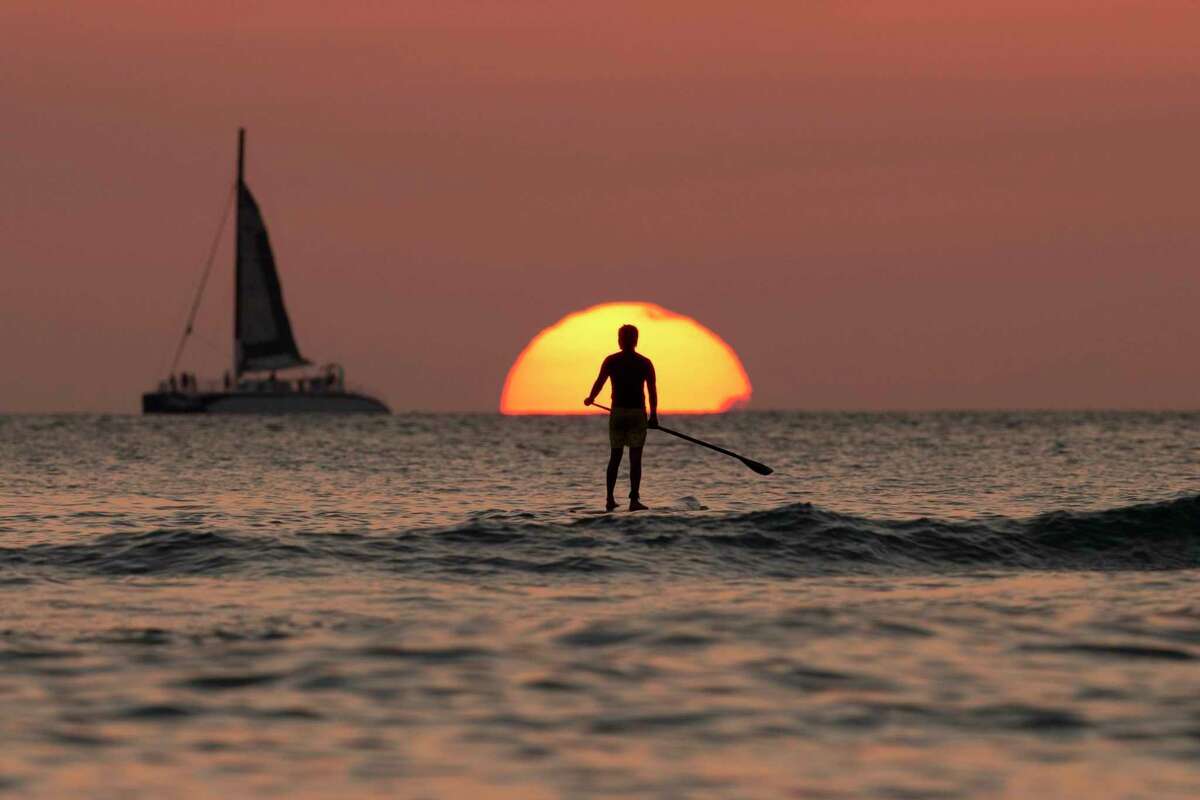 FILE - In this Dec. 31, 2013, file photo, a paddleboarder looks our over the Pacific Ocean as the sun sets off of Waikiki Beach, in Honolulu. When you?’re just starting out, even a weeklong vacation might seem like a one-way ticket to credit card debt ?— especially if you have a modest income or lack access to paid time off. But with the right moves, you can budget for travel without going into the red. (AP Photo/Carolyn Kaster, File)