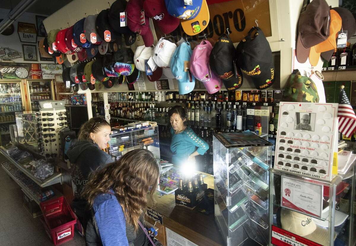 Victoria Um serves customers in the dark at the Calistoga Smoke Shop on Monday. Residents’ routines and tourists’ plans were upended when PG&E shut down power to Calistoga and other towns Sunday.