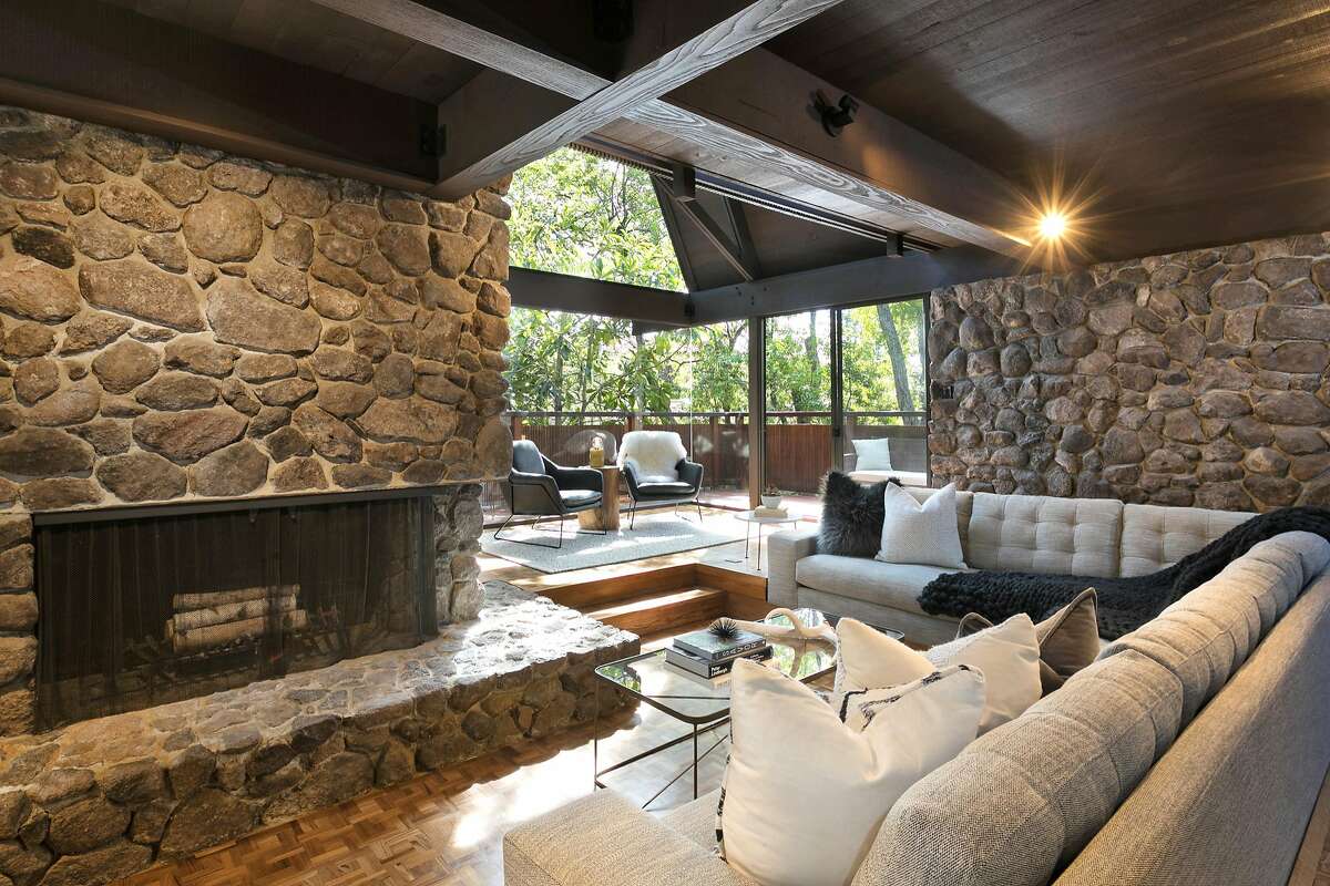 The living room’s stone fireplace at 252 The Uplands in Berkeley offers a sitting ledge and stands beside a sitting area that opens to a deck.