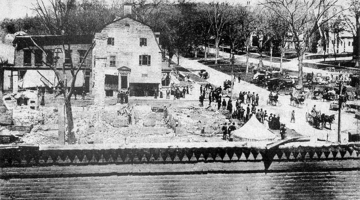 The Great Fire of May 1902 swept through the business district of New Milford, destroying much of the Railroad to Main streets and Bridge to Bank streets block in smoke and ashes. This view looking north shows many of the townsfolk milling around the ruins, even as a shantytown grew on the south end of the Village Green to provide temporary homes to the displaced merchants. The large building at the north corner of Bank and Main is the United States Hotel,which survived the blaze only to be razed during the 1920s to make room for a pharmacy. On the nearer street corner are the remains of the New England House Hotel, the other half of the village center's proud bookends hotels of the era. If you have a