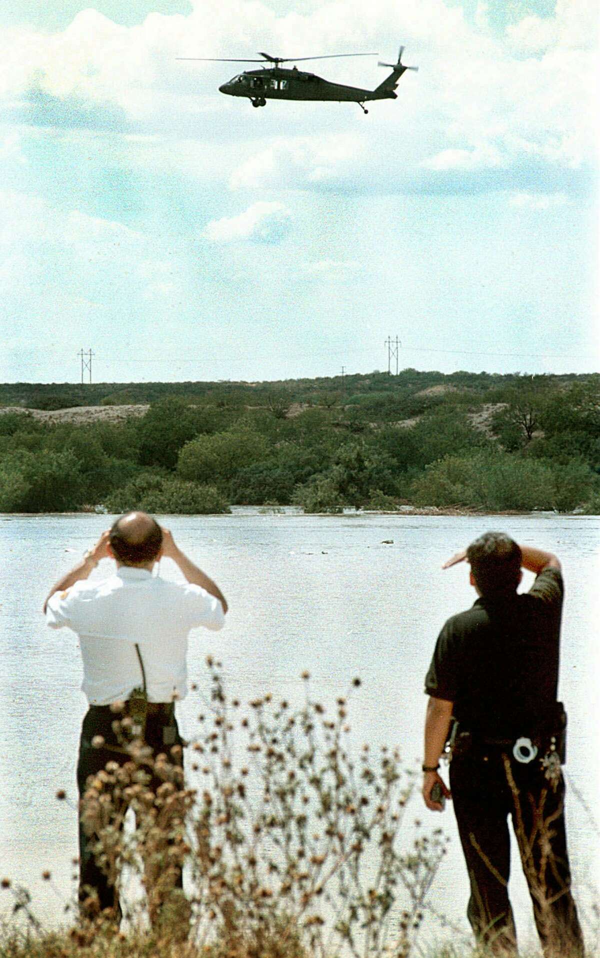 Laredo, Texas fire and police officials watch from the banks of the flooded Rio Grande as a National Guard helicopter searches for an individual reported floating along the rising river, Wednesday, Aug. 26, 1998. Local rescue teams have been dispatched throughout the day to the river to search for the reported drowning victims. The rescue teams so far have been unsucessful in finding any victims.