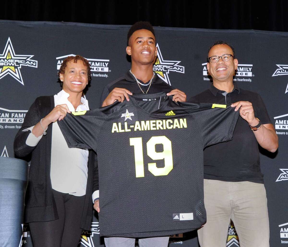 With his smiling parents, Dr.Cassandra Tribble, left, and Claude Johnson by his side, Brunswick School football player, Cornelius Johnson, center, a wide receiver, holds his All-American football jersey from the organizers of the national All-American Bowl by American Family Insurance during a presentation ceremony at Brunswick School where Johnson plays and is a senior, Greenwich, Conn., Tuesday, Oct. 16, 2018. The bowl game Johnson will play in will be played in San Antonio, Texas, on January 5, 2019.