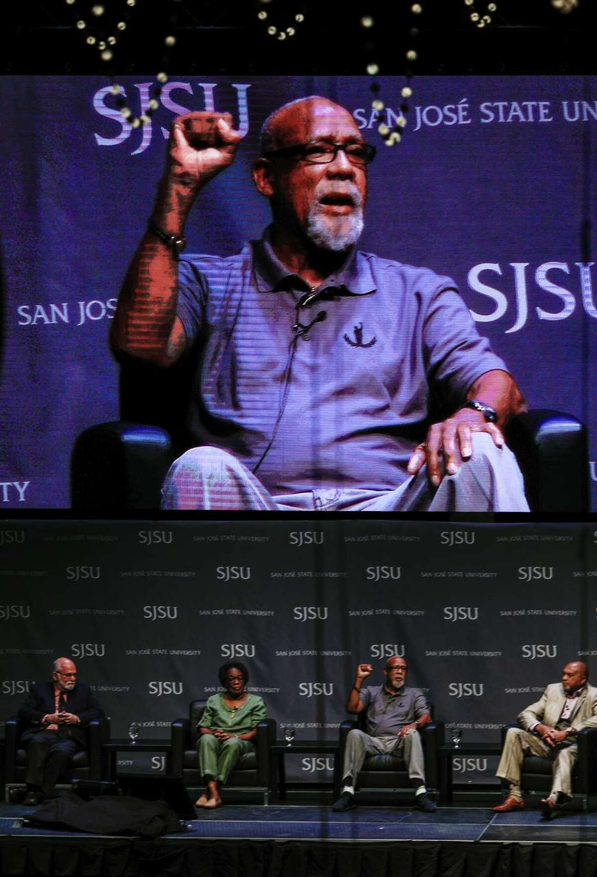 Joint caption: LEFT: 1968 Olympic athlete Juan Carlos (center) speaks about his experience during the Mexico City Olympics in the Words to Action panel at San Jose State University in San Jose, California, on Wednesday, Oct. 17, 2018. RIGHT: FILE - In this Oct. 16, 1968 file photo, extending gloved hands skyward in a Black power salute as a form of racial protest, U.S. athletes Tommie Smith, center, and John Carlos stare downward during the playing of national anthem after Smith received the gold and Carlos the bronze for the 200 meter run at the Summer Olympic Games in Mexico City. While the games were marked by dissent, today's situation in Mexico is much more chaotic with a government that is barely in control of many aspects of society, battered by violent drug cartels that are often supported by rogue cops and mayors. (AP Photo, File)