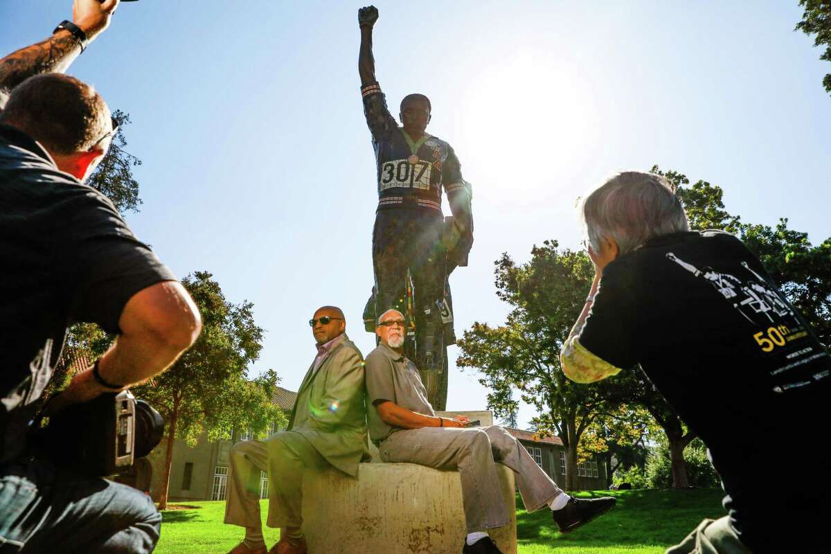 Tommie Smith (left) and John Carlos sit below the statue that honors their iconic protest at the 1968 Mexico City Olympics.