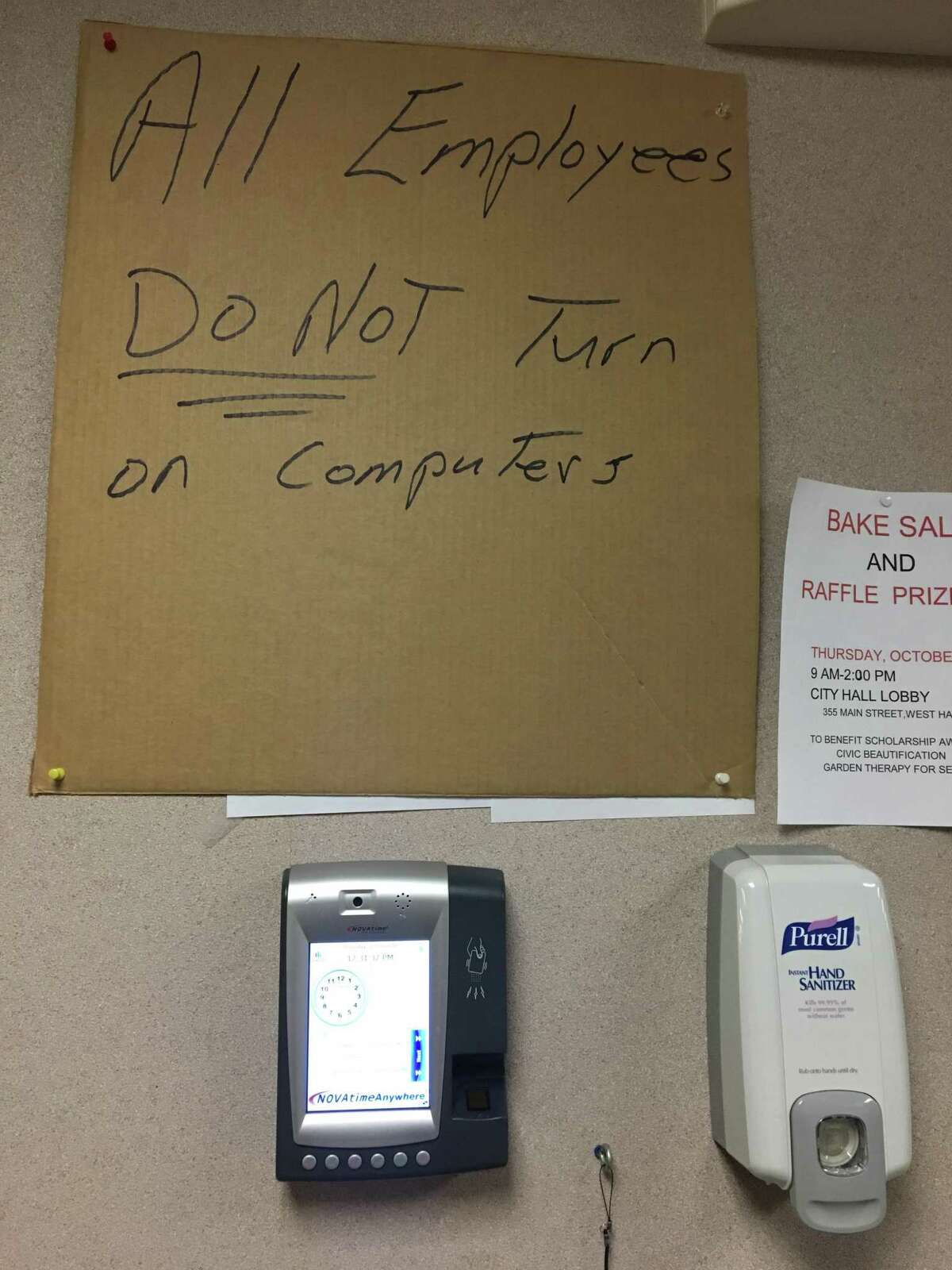 A hand-lettered sign on a corrugated box panel hung above a time clock on the 2nd floor of West Haven City Hall cautions employees not to turn on their computers while the effects of a cyber attack are mitigated.