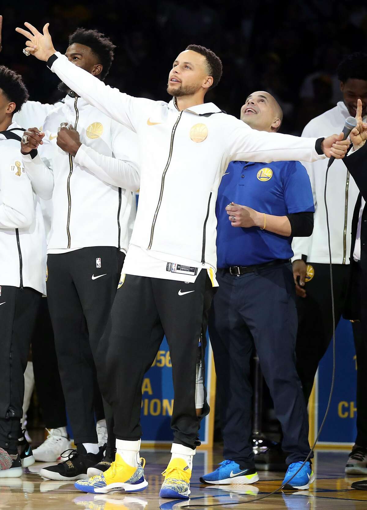 Golden State Warriors' Stephen Curry and equipment manager Eric Housen watch as 2018 NBA Championship banner is unveiled during ceremony before Opening Night game against Oklahoma City Thunder at Oracle Arena in Oakland, Calif. on Tuesday, October 16, 2018.