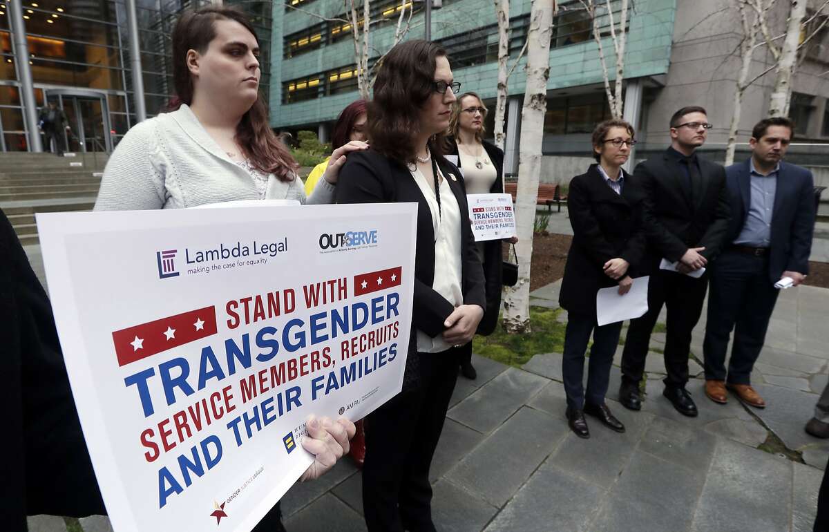 FILE - In this March 27, 2018 file photo, plaintiffs Cathrine Schmid, second left, and Conner Callahan, second right, listen with supporters during a news conference in front of a federal courthouse following a hearing in Seattle. Transgender-rights activists are angered at moves by President Donald Trump and his administration to undermine gains achieved before his election. Trump is seeking to ban transgender people from military service, although that effort has stalled in court. (AP Photo/Elaine Thompson)