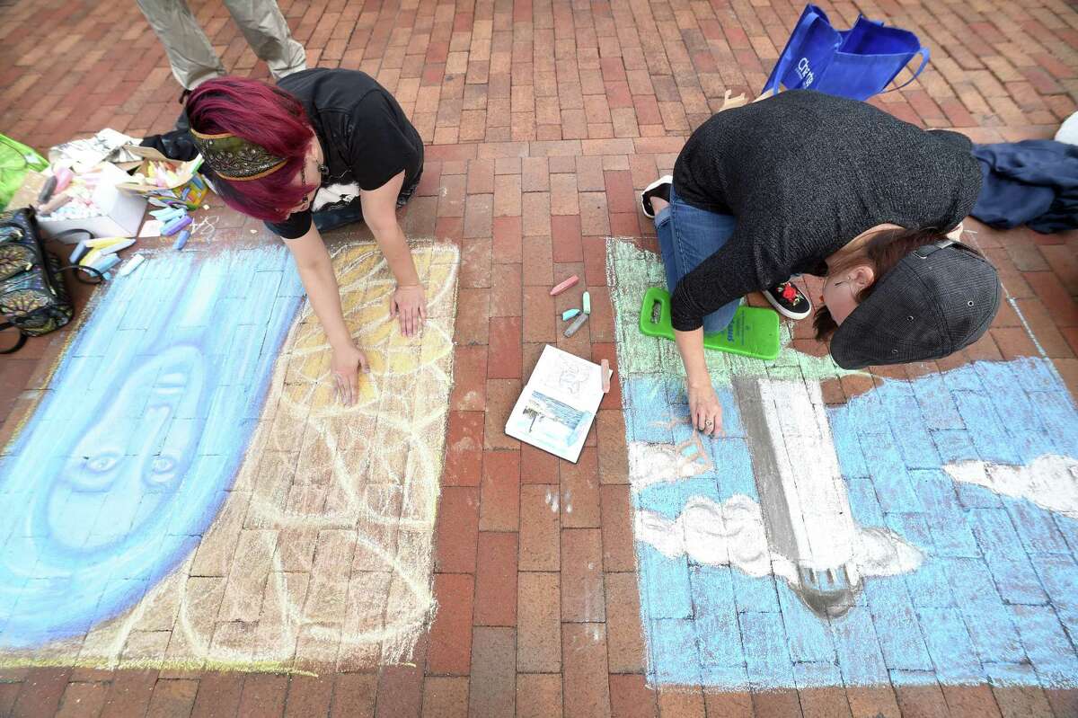 Audrey Kantrowitz (left) of Cheshire draws a blue fairy next to Carlene Sisbarro of Derby who is drawing the New Haven lighthouse with the sea monster, Kraken, during the New Haven Chalk Art Festival on the Broadway Island in New Haven on October 20, 2018.