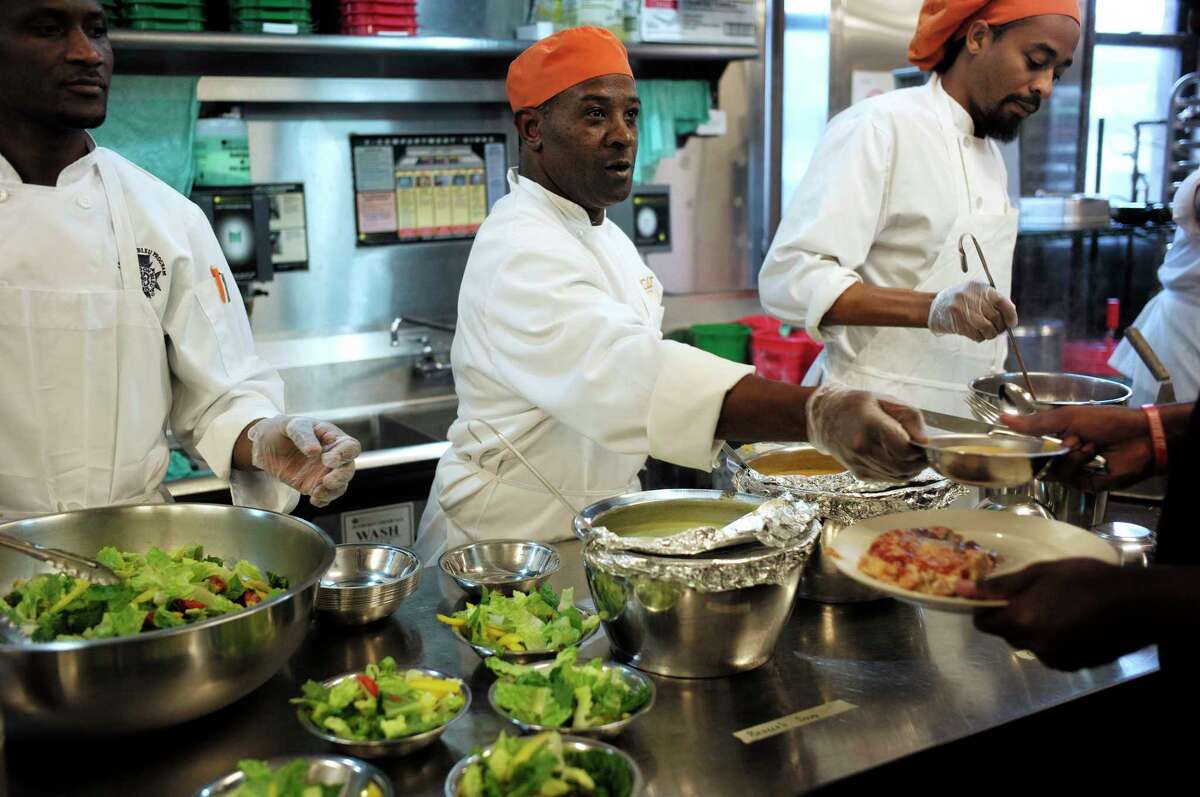 In this Tuesday, Oct. 2, 2018 photo Phillip Oliver, of New Bedford, Mass., center, in recovery from opioid addiction, helps serve a meal in a culinary training program at the New England Center for Arts and Technology, in Boston. In Massachusetts, with Medicaid expansion already paying for opioid addiction treatment, emergency money from Congress goes largely toward recovery services. The state has chosen to use its federal money for those in long term recovery to pay for things like housing, and job training. (AP Photo/Steven Senne)