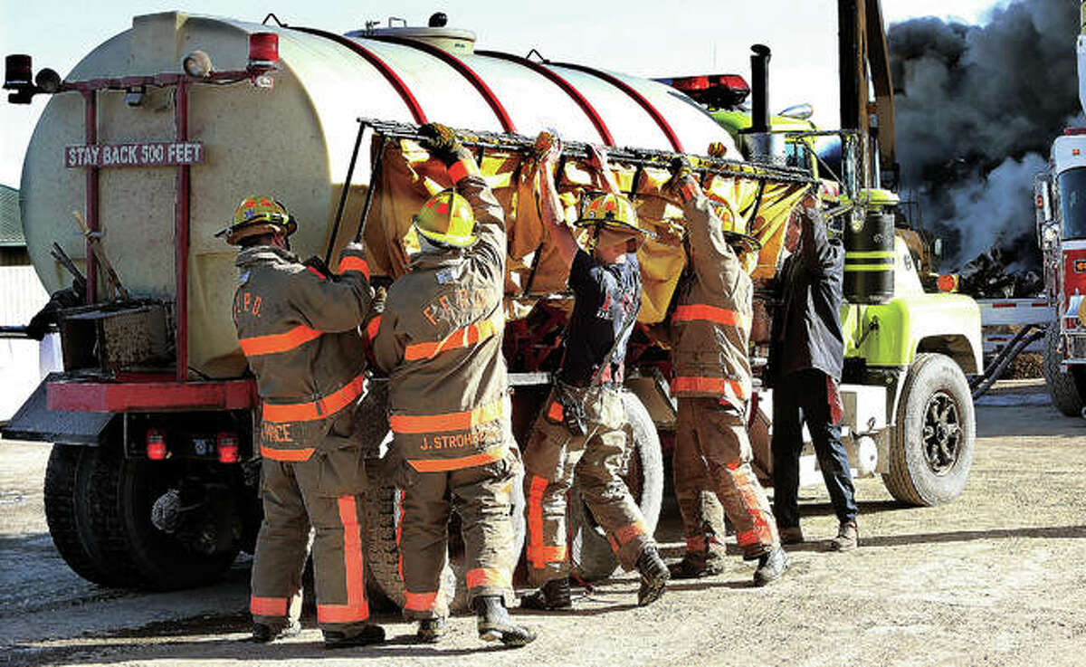 It took a small army of rural firefighters to extinguish the burning cars and other debris piled about 50 feet high. Firefighters work to unload one of the storage tanks they use to hold portable water in rural areas where no fire hydrants are nearby. The closest hydrant Tuesday was four miles away.