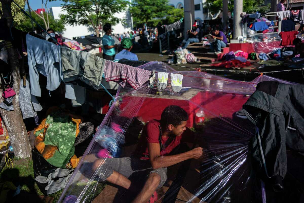 A Central American sits under a makeshift tent in Huixtla on Tuesday. The normal route north for migrants requires paying thousands of dollars to cartel-linked smugglers.