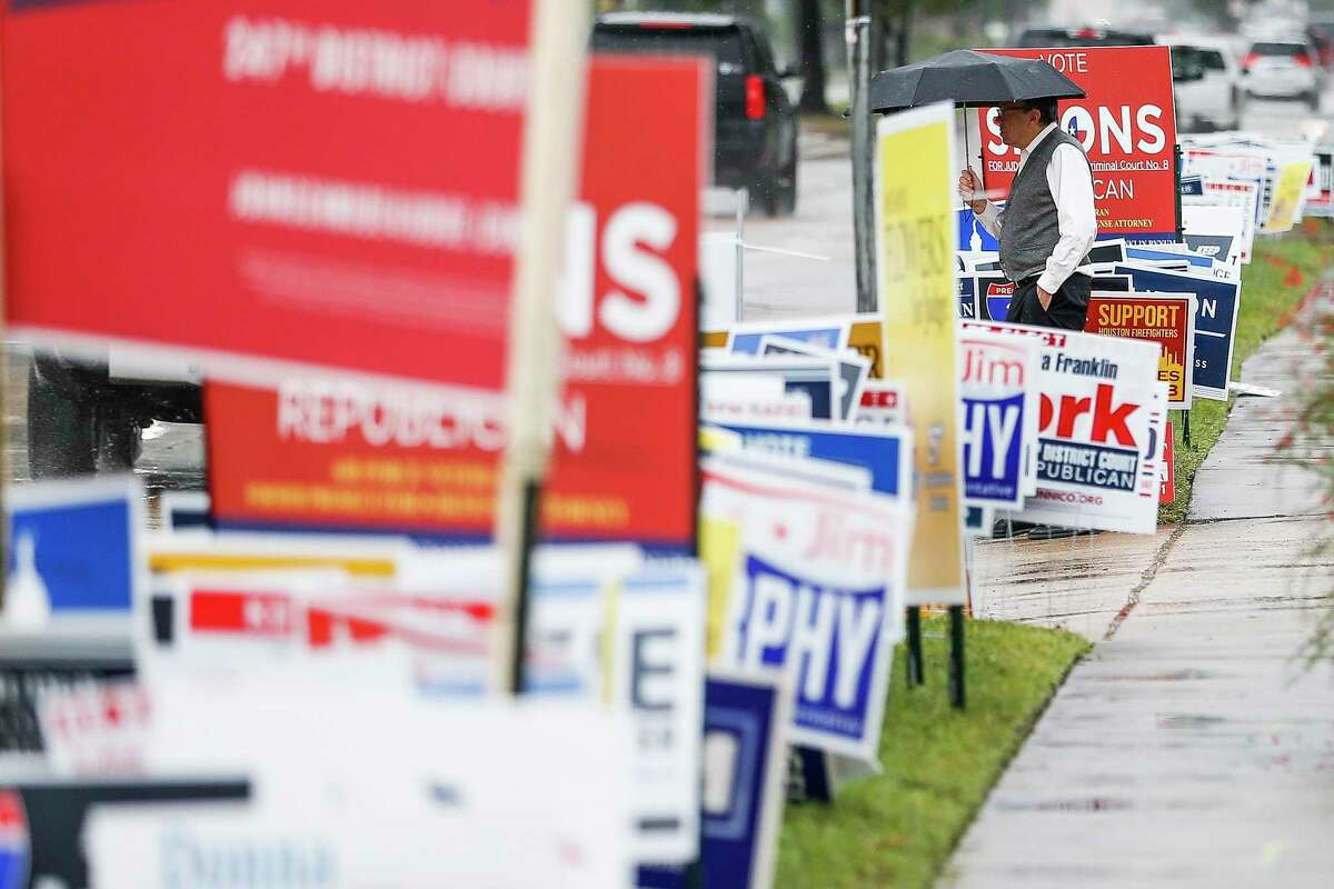A man walks past campaign signs as people brave the rain to head to the polls for the second day of early voting at the Trini Mendenhall Community Center Tuesday Oct. 23, 2018 in Houston.