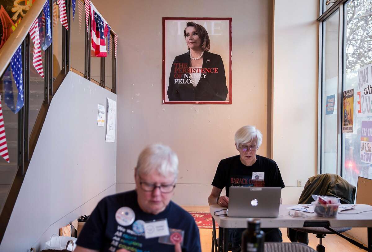 Two volunteers man the front door while sitting under a painted replica portrait of House Minority Leader Nancy Pelosi at the Red to Blue campaign office established by Pelosi in San Francisco, Calif. Thursday, Nov. 1, 2018.