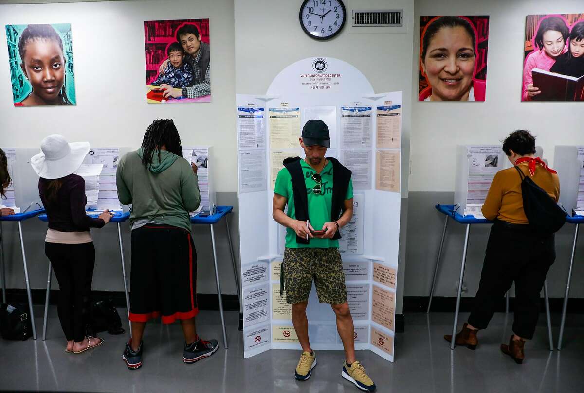 Tuan Nguyen (center) checks his phone as others cast their vote at the Registrar of Voters office in Oakland, California, on Monday, Nov. 5, 2018.