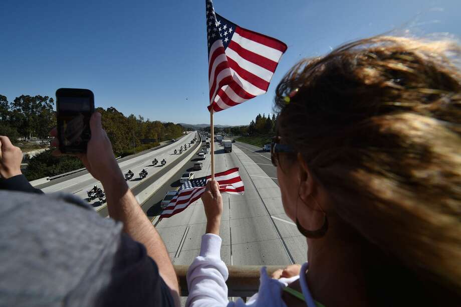 People line an overpass to see a motorcade procession transports the body of Sheriff's Sergeant Ron Helus, the first victim named in the mass shooting at a country bar in Thousand Oaks, California, November 8, 2018 - The gunman who killed 12, including Helus, people in a crowded California country music bar has been identified as 28-year-old Ian David Long, a former Marine, the local sheriff said Thursday. The suspect, who was armed with a .45-caliber handgun, was found deceased at the Borderline Bar and Grill, the scene of the shooting in the city of Thousand Oaks northwest of downtown Los Angeles. Photo: ROBYN BECK/AFP/Getty Images