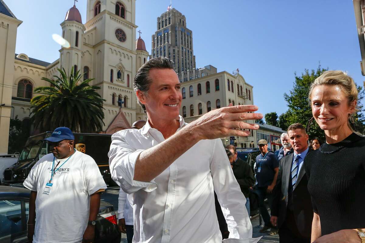 Gov. elect Gavin Newsom waves at supporters as he and wife Jennifer Siebel Newsom walk to St. Anthony's Dining Room to help serve lunch service on Thursday, November 8, 2018 in San Francisco, Calif.