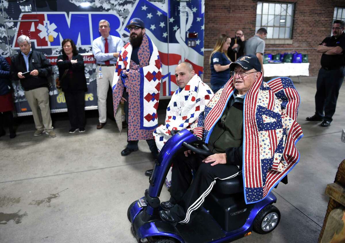 Left from center, EMT dispatcher for AMR and former Navy medic Billy Richmond, AMR clinical manager and Army veteran Mike Turcio and Turcio's grandfather, Korean War veteran Charles Turcio, are wrapped in hand-made quilts from Quilts of Valor during a ceremony following a breakfast for veterans at American Medical Response headquarters in New Haven on November 9, 2018.