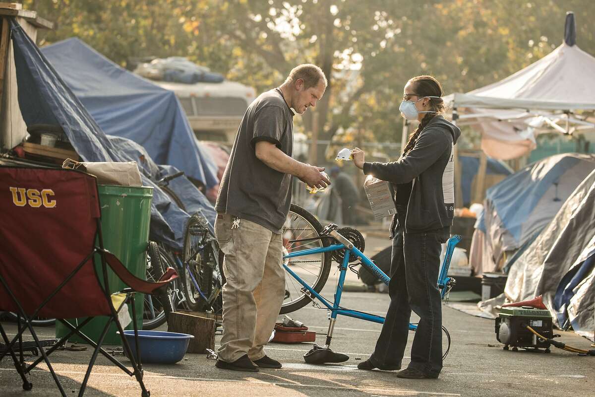Whitney Moses hand out smoke masks to Tim Green, an ex-Marine at a homeless encampment near Home Depot at Alameda Ave and High Street on Monday, Nov. 12, 2018, in Oakland, Calif.