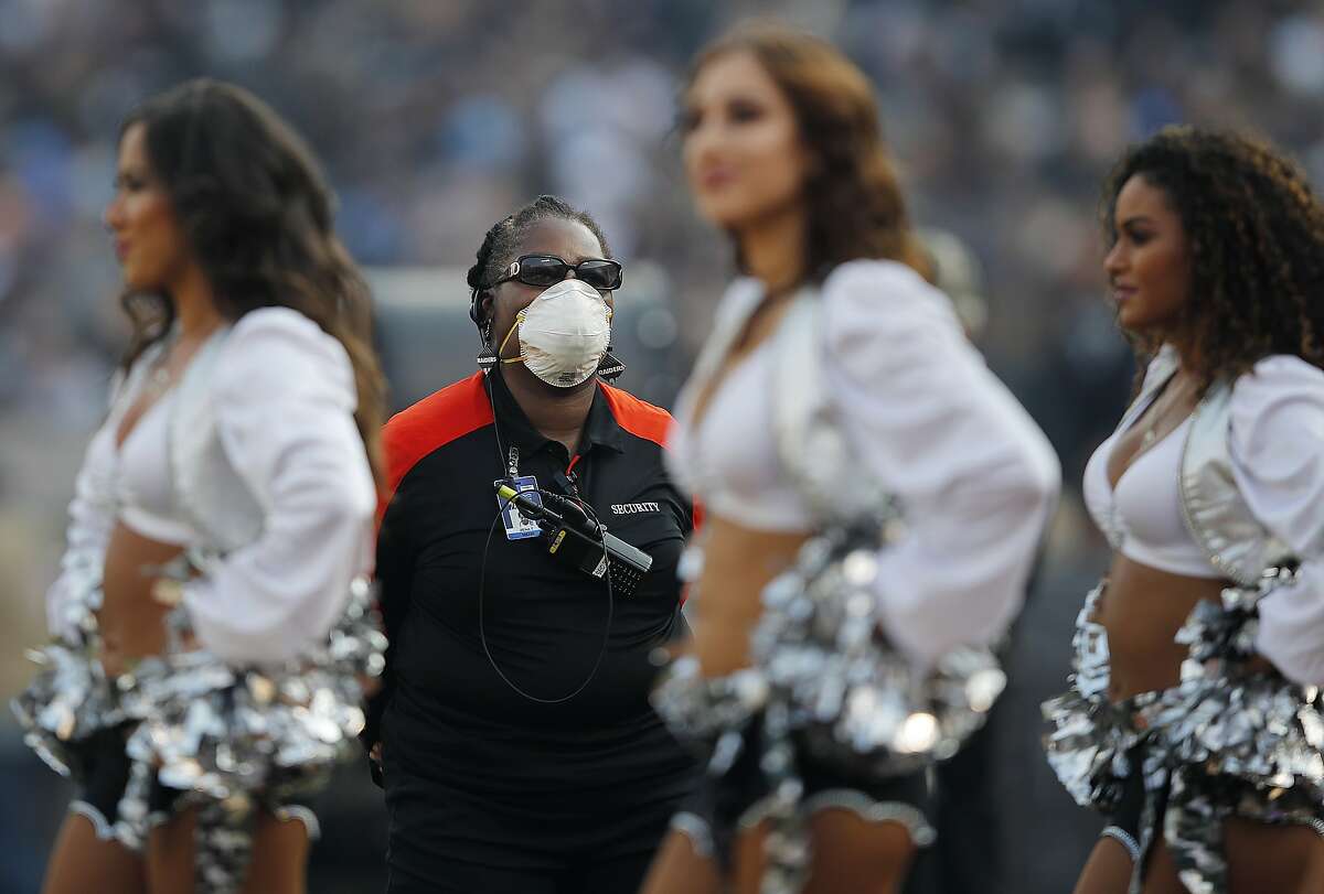 A security guard wears a mask on the field due to wildfires during the second half of an NFL football game between the Oakland Raiders and the Los Angeles Chargers in Oakland, Calif., Sunday, Nov. 11, 2018. (AP Photo/John Hefti)